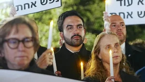 A group of people hold candles and signs during a vigil or memorial event.