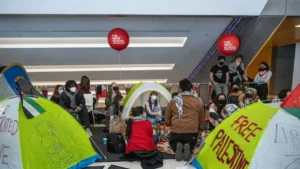 A group of people are gathered in a tented protest at The New School, advocating for Palestinian freedom and other causes.