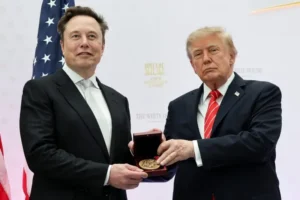 The image shows two individuals in formal attire, one presenting a medal to the other, with an American flag and a backdrop indicating a formal event at the White House.