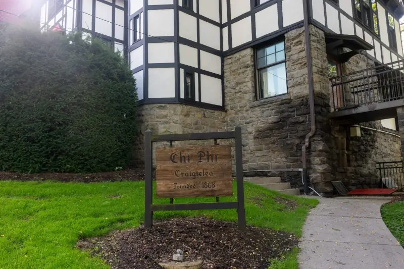 The image shows a sign for Chi Phi Craigteleo, founded in 1868, in front of a historic stone building with a Tudor-style facade.