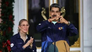 The image shows two individuals in matching jackets, one making a heart shape with their hands, in a setting decorated with Christmas elements.