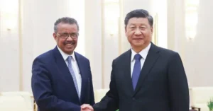 Two individuals in formal attire are shaking hands in a well-lit indoor setting, suggesting a diplomatic or official meeting.