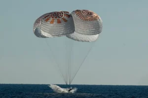 A spacecraft is seen landing in the ocean with its parachutes fully deployed.