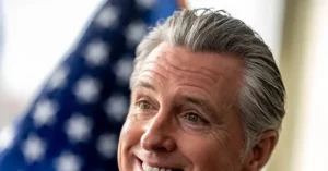 The image shows a person smiling with an American flag in the background.