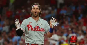 A baseball player in a Philadelphia Phillies uniform celebrates with a surprised expression and raised hands.