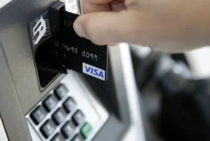 A person is inserting a Visa credit card into an ATM machine.