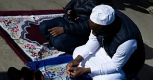 Two individuals are engaged in a religious or spiritual activity on a prayer mat outdoors.