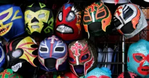 The image shows a collection of colorful wrestling masks, each with unique designs and patterns, displayed on a rack.