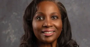 The image shows a close-up portrait of a smiling individual with long, dark hair against a neutral background.