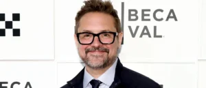 The image shows a man wearing glasses and a suit, smiling in front of a backdrop with the text "BECAL."