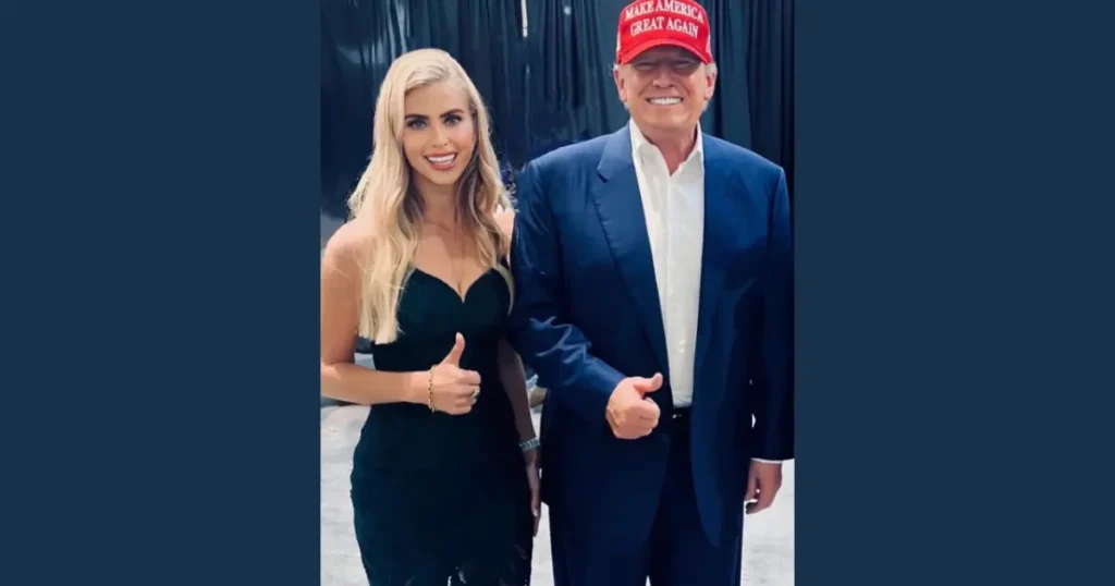 The image shows two individuals posing together, one wearing a "Make America Great Again" hat and the other in formal attire.