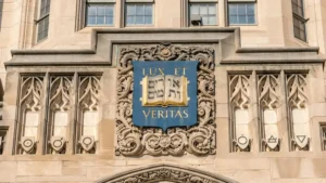 The image shows a decorative stone facade with the Latin phrase "LUX ET VERITAS" and Hebrew script, symbolizing light and truth, likely representing a university or institution.