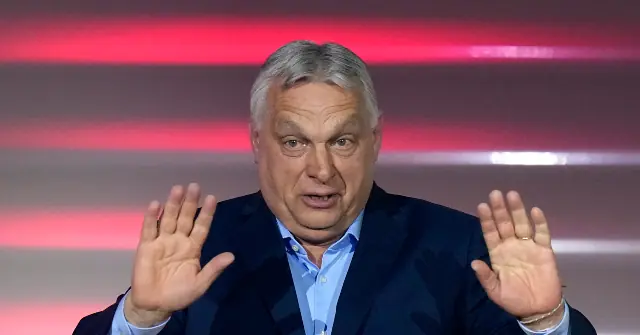 The image shows a man in a suit with his hands raised, possibly gesturing or speaking emphatically.