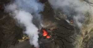 The image shows an aerial view of a volcanic eruption with lava and smoke billowing into the air.