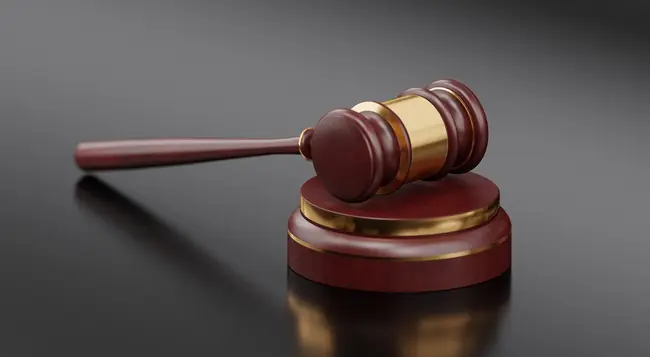 The image depicts a classic wooden gavel, symbolizing authority and justice, resting on a dark reflective surface.