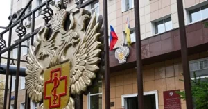 The image shows a building entrance adorned with a double-headed eagle emblem and a red cross, with flags of Russia and Ukraine displayed above the entrance.