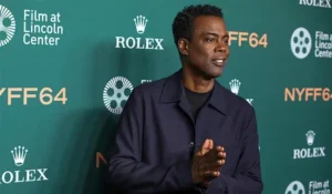 The image shows a person at the New York Film Festival (NYFF64), standing in front of a backdrop featuring logos for Rolex and Film at Lincoln Center.