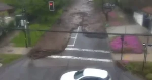 A flooded street with a red traffic light and a partially submerged car is visible, indicating severe flooding in the area.